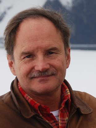 Smiling friendly looking man with brown hair and graying mustache.