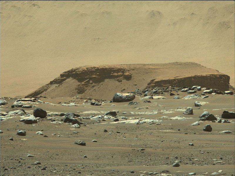 Rocky outcrop with larger hill behind it and boulders at its base.