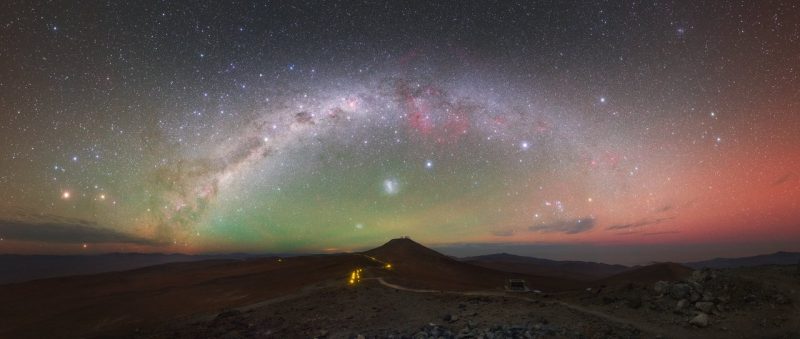 Desert landscape, glowing arch of Milky Way above with two small, fuzzy bright patches near it.