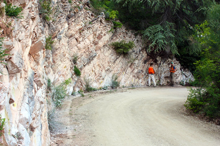 Men stand on a street and examine rock layers in the steep street section.