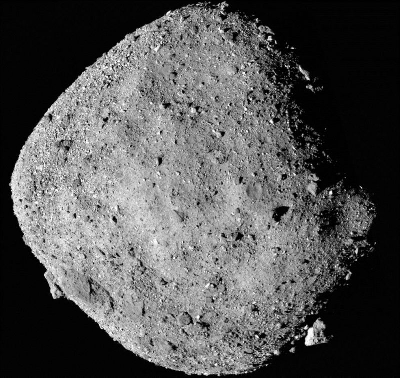 Squarish gray asteroid with rough surface scattered thickly with individual rocks.