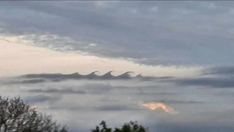 Sharply-defined, dark, wave-shaped clouds in gap in cloudy sky.