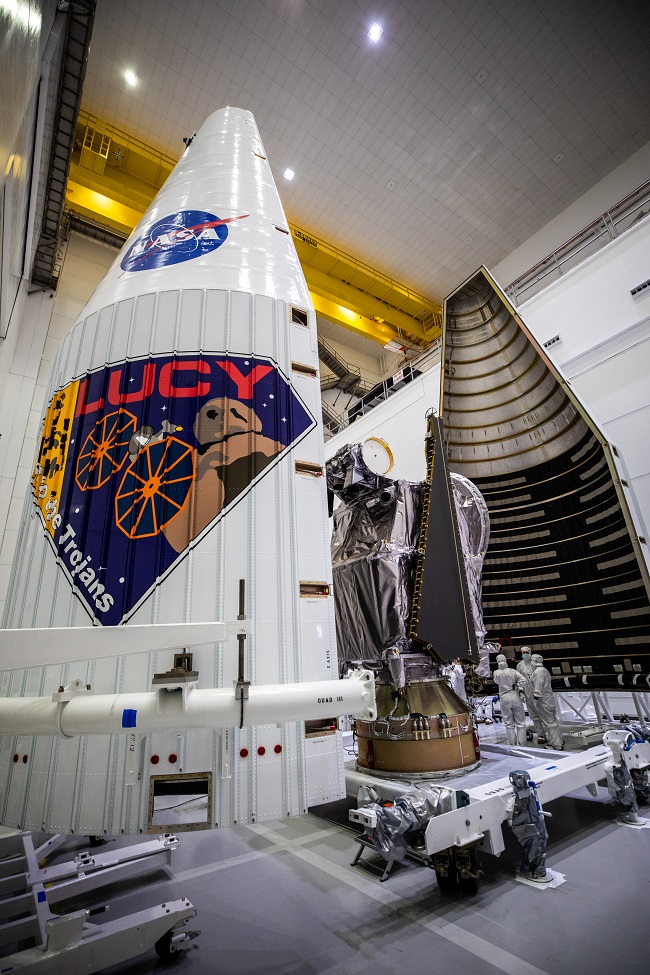 Folded spacecraft between two tall halves of a rocket nose in a large clean room.