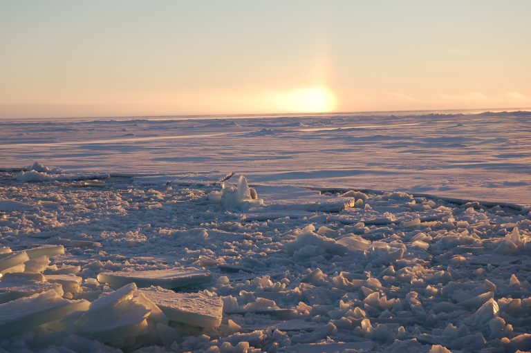 Sun setting at horizon of vast field of ice.
