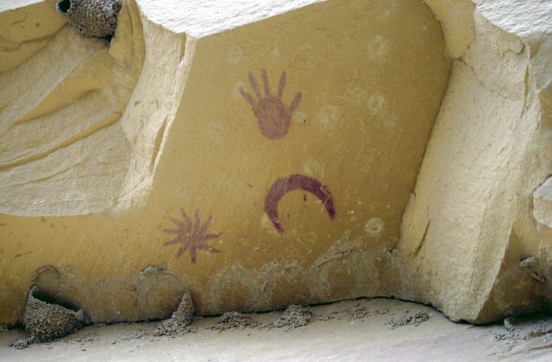 Rock art of a sun, a hand, and a crescent.