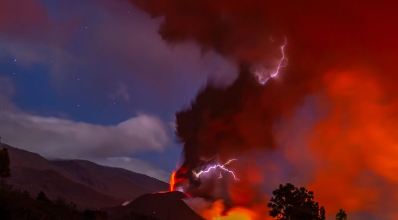 Ash clouds glowing red from volcanic eruption with lightning in the clouds.