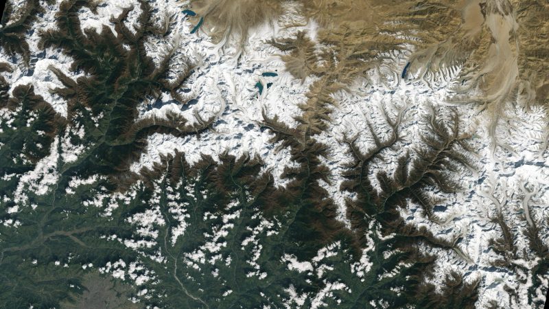 Landsat 9: Feather-like patterns of white snow-capped mountains with tan, brown and teal valleys.