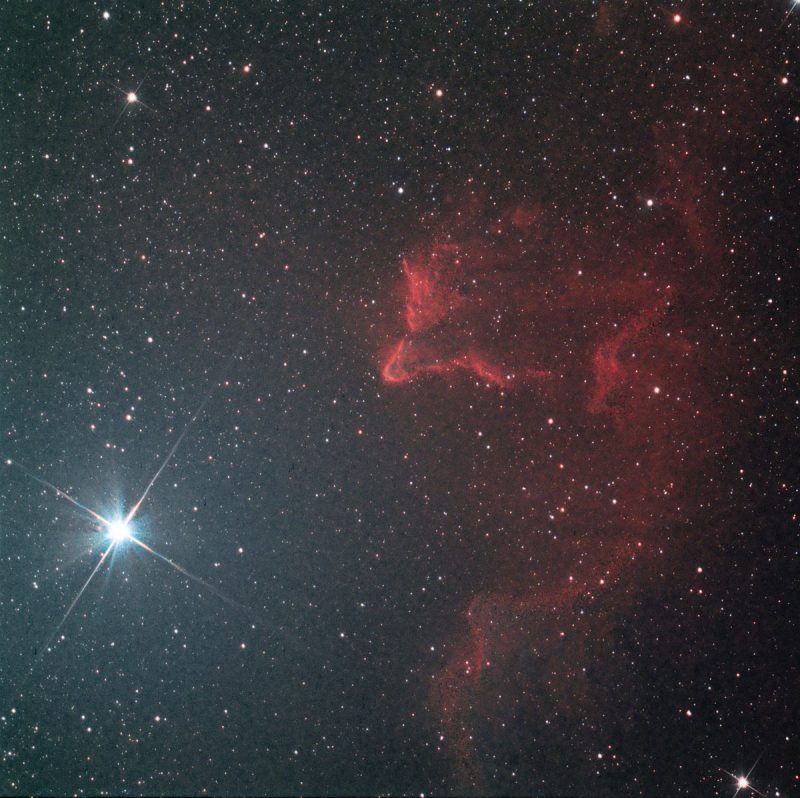 Bright star with spikes at left and reddish nebulosity at right.