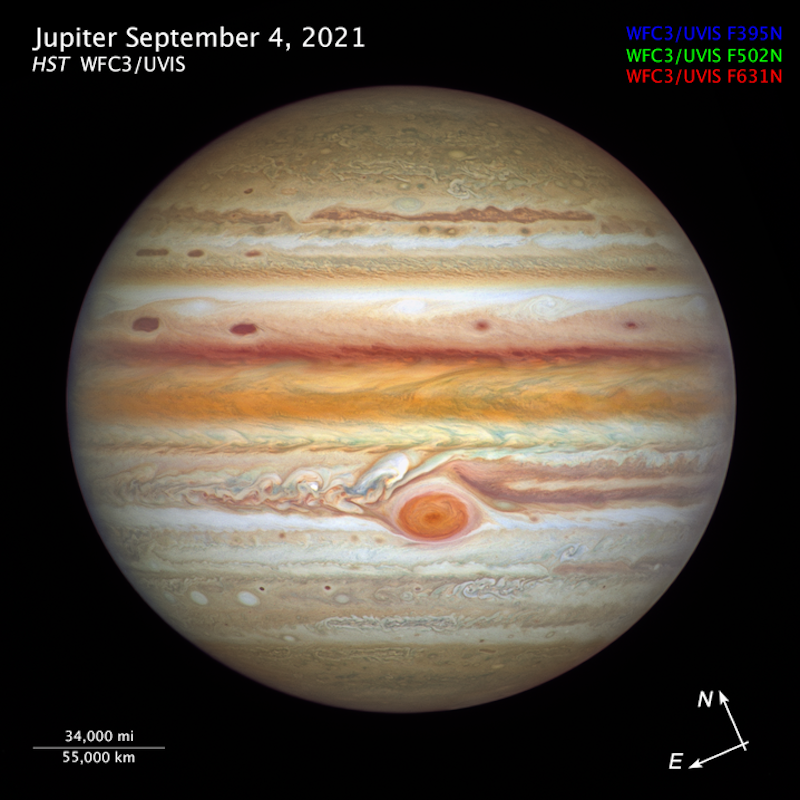 Jupiter with colorful, swirly banded atmosphere, spotted with oval storms. Titles and scale of size.
