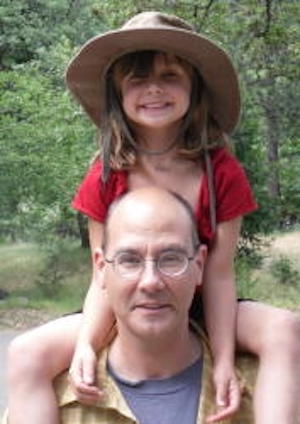 Man with little girl in large hat sitting on his shoulders, and trees in background.