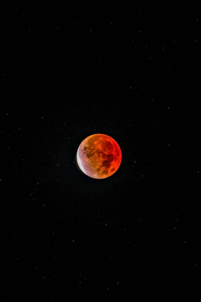 Orange moon with sliver of white on one side, and stars in the background.