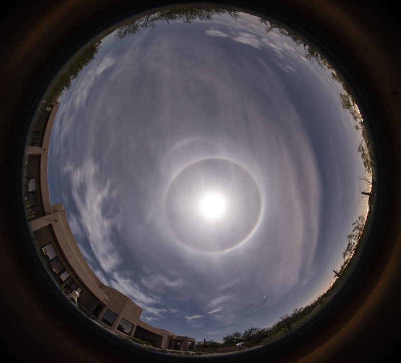 Rare moon halo: Fisheye overhead view of wispy clouds with bright circle of moon and one bright ring and two off-center rings.