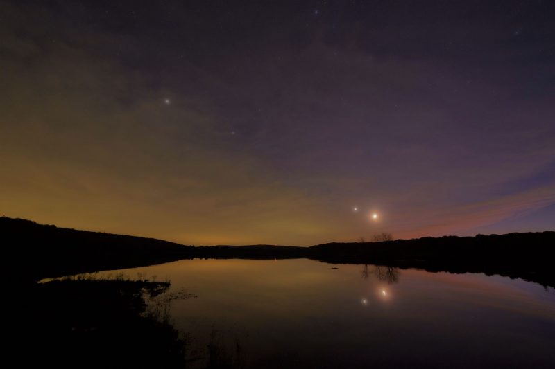 Lake with thin clouds and moon at lower right, then Venus, Saturn and Jupiter in line extending to upper left.