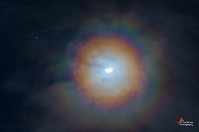 Colorful ring and thin clouds around a gibbous moon.