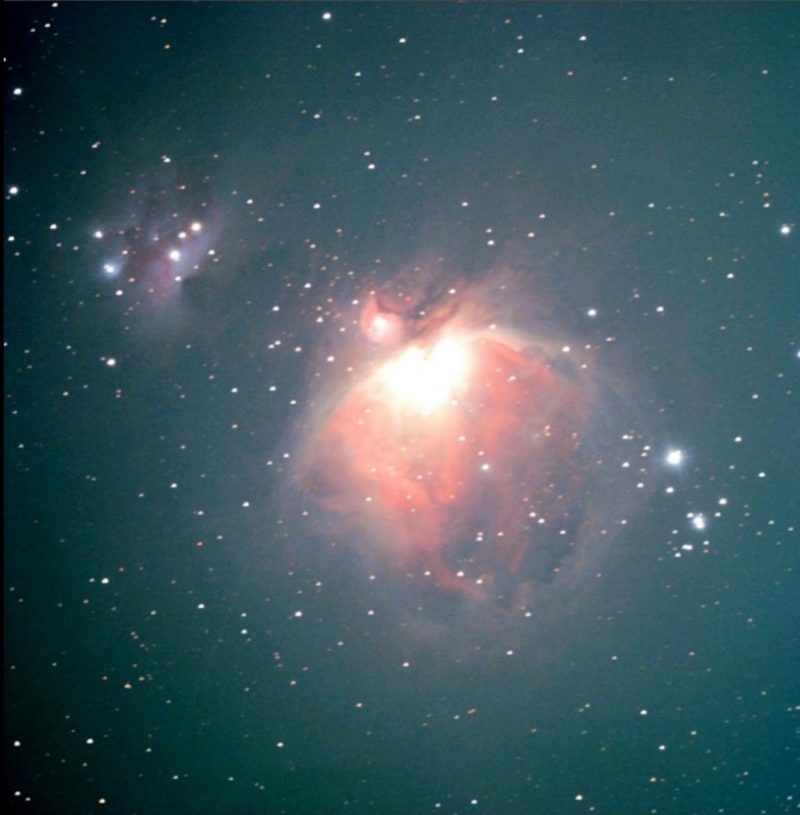 Bright light in semicircular orangish-pink cloud. Above, a smaller bluish nebula with stars in it.