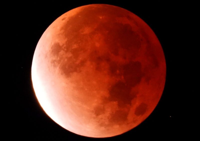 Lunar eclipse photos: Reddish moon with a white glow on the lower left side. 
