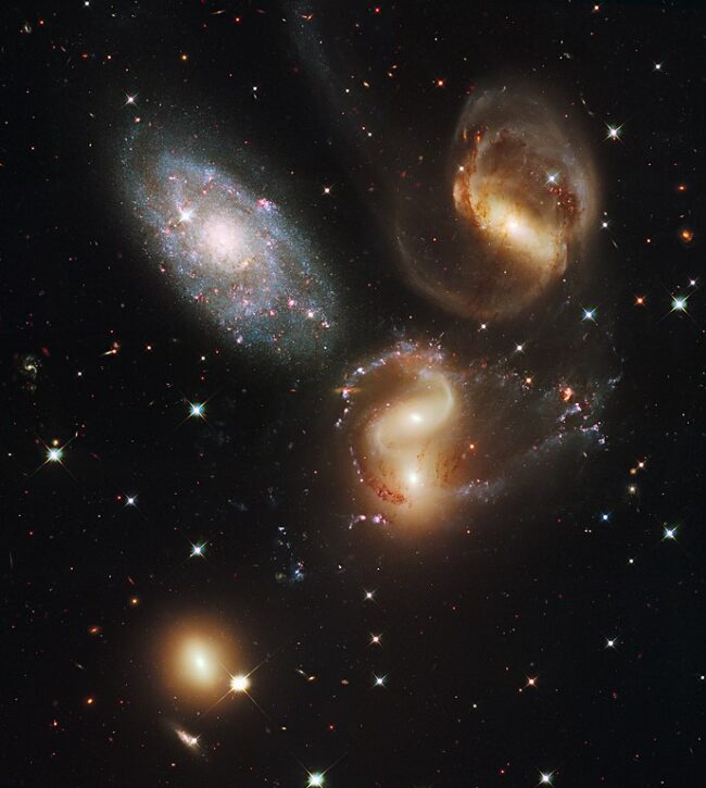 A cluster of galaxies including large colorful spirals and two galaxies merging.