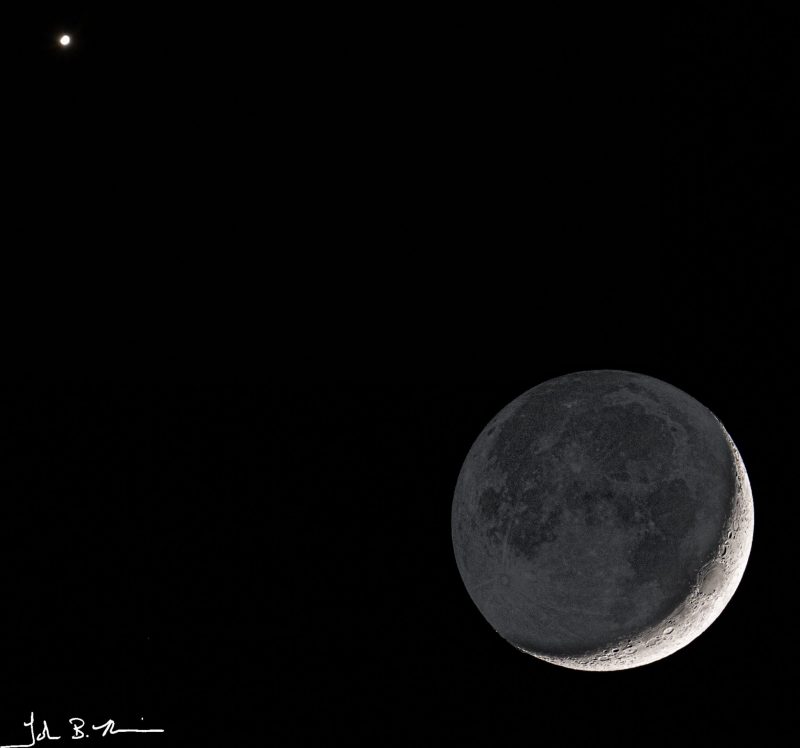 On black background, a small white dot at top left, crescent moon and earthshine at bottom right.