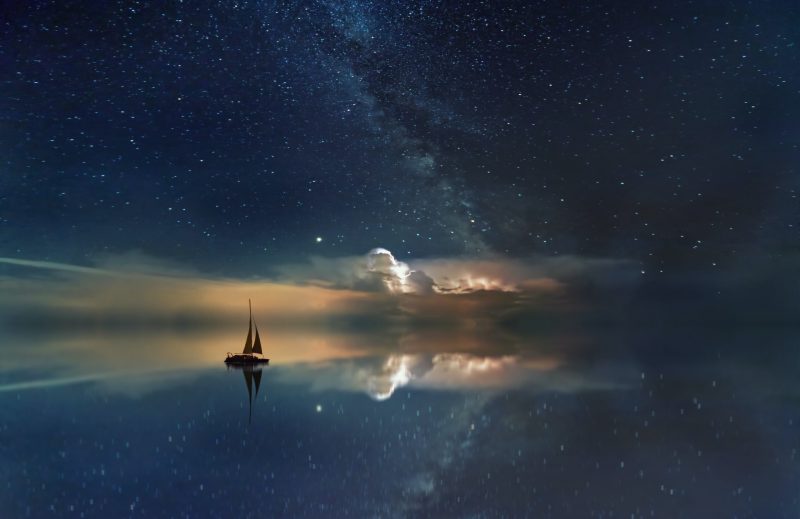 Top 10 stories of 2021: Sailboat on a placid lake reflecting distant storm-lit clouds and Milky Way.