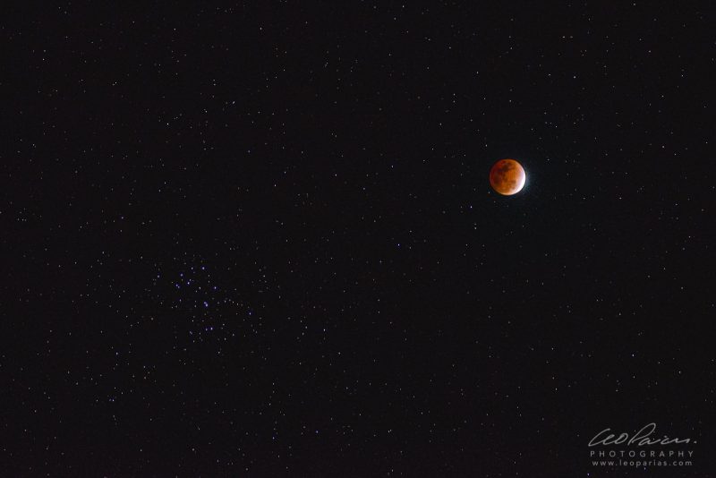 Reddish moon upper right with sliver of white along one side, smattering of stars lower left.