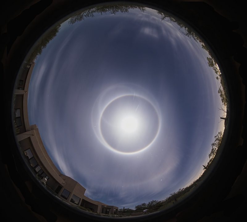 Fisheye overhead view of wispy clouds with bright circle of moon and one bright ring and two off-center rings.