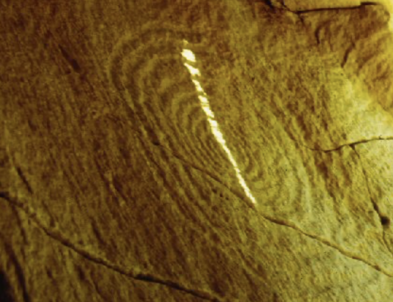 Spiral rock art, with a slice of light cutting straight across it.