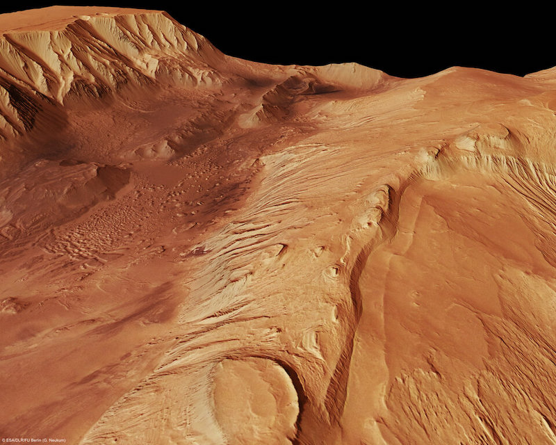 Bird's-eye view of reddish terrain with valley and cliffs.