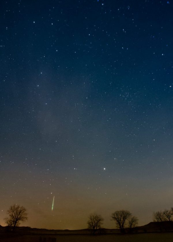 In dark blue sky with stars, a thin green vertical streak near the horizon.