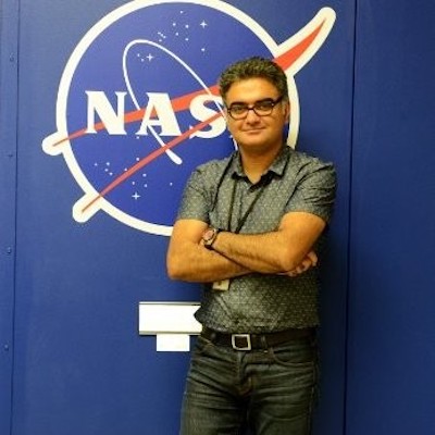 Man with eyeglasses and his arms folded, standing in front of big NASA logo.