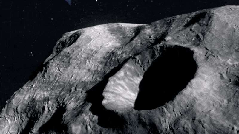Yellow boxy spacecraft passing in front of deep, shadowed crater on irregular space rock.