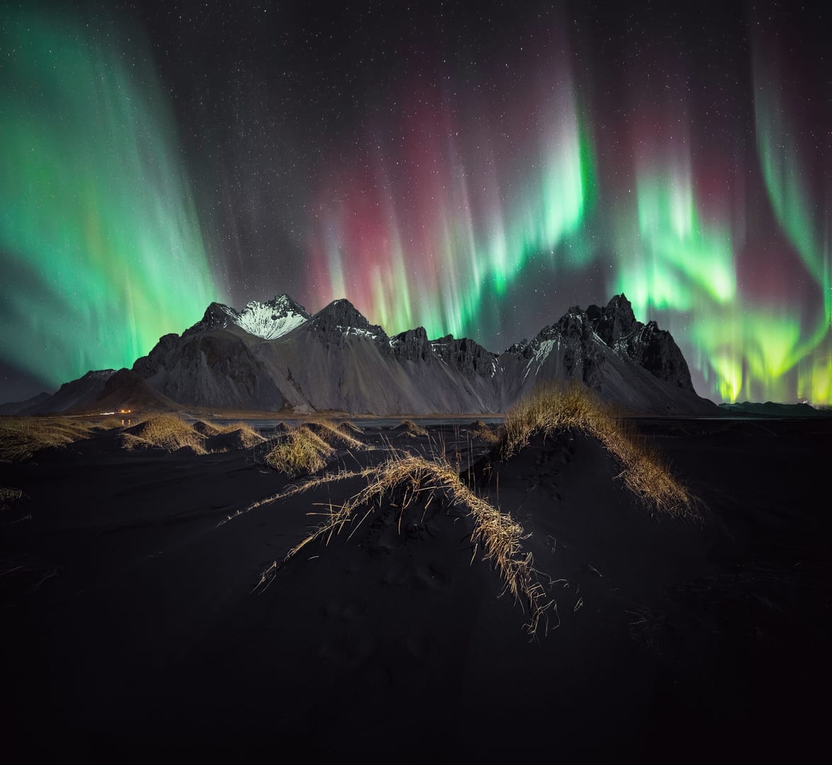 Green and pink flames of aurora over a long mountain range.
