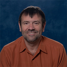 Man in orange polo shirt with hair combed forward.