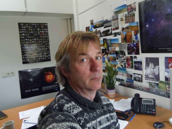 Man looking warily at camera with astronomy photos on the walls.