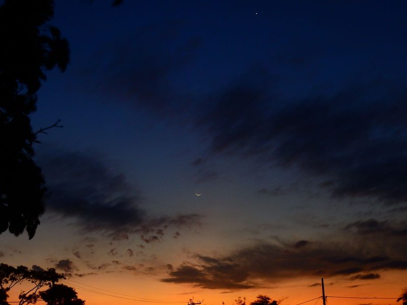Crescent moon in sunset, point of light above.
