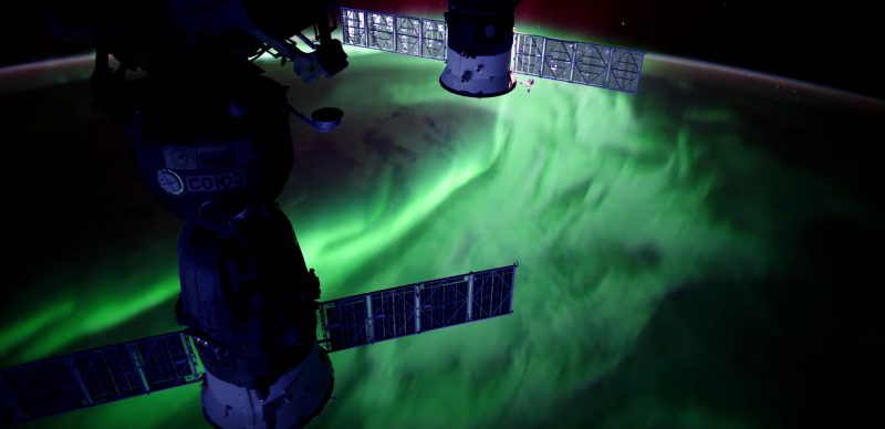 Greenish swirls of light below solar panels on the space station.