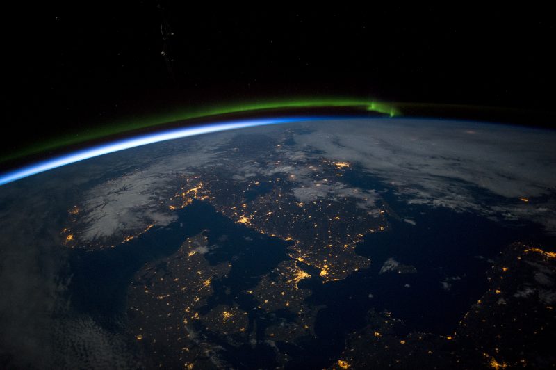 Black night orbital view of planet Earth centered on Sweden with gold lights of cities and green aurora.