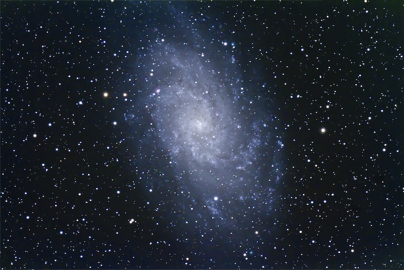 The Triangulum Galaxy appears as a nebulous white pinwheel-shaped spiral galaxy with many stars in the foreground. 