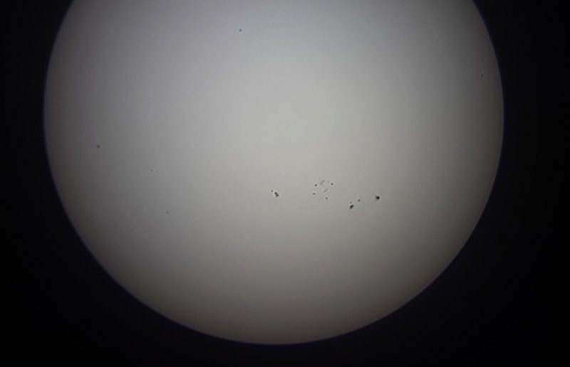 Black and white view of the sun with dots strung across near the middle.