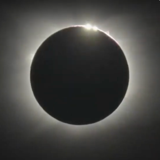A black circle with light radiating from behind it and bright spots on the top edge.