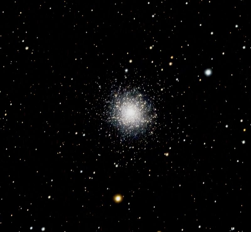 Bright white round cluster of thousands of stars at center with smattering surrounding in black sky.