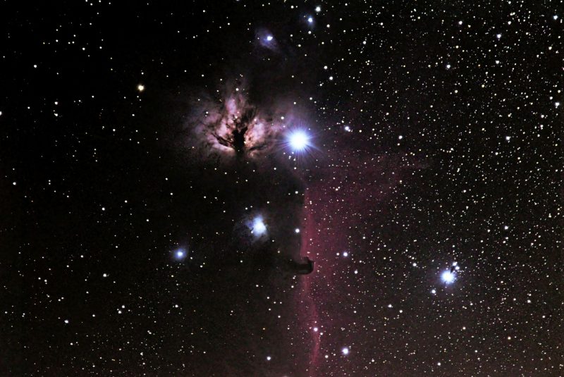 Black background with white stars and pink light behind black clouds.