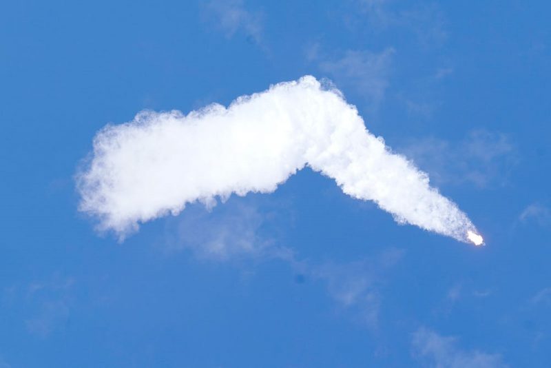 A rocket with a large white cloud trail against a bright blue sky.