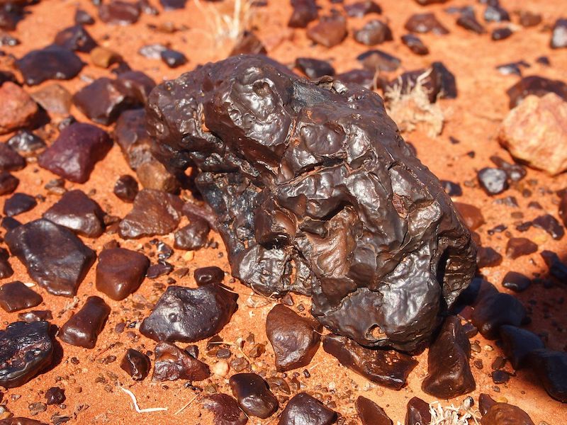 Dark shiny rocks on reddish soil.