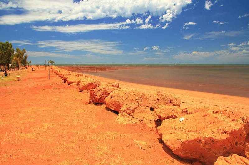 Hottest temperature on record: Red sand on coast with blue sky and white puffy clouds above.