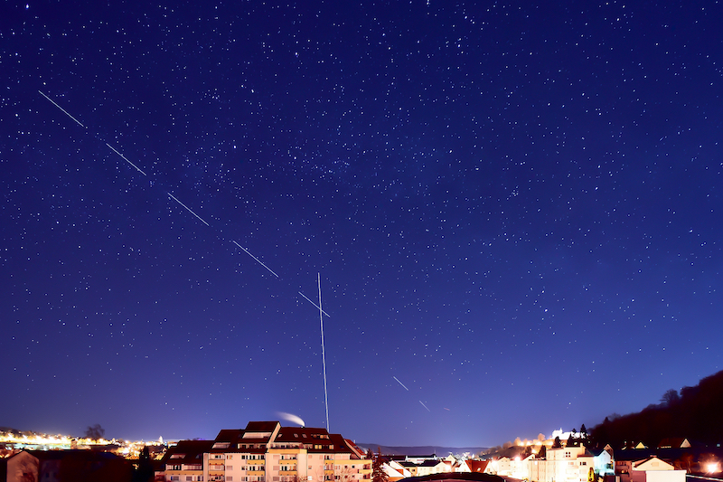 A starlink satellite leaves a trail on a dark blue night sky full of stars.