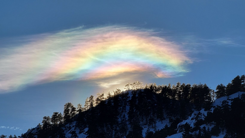 Sun is behind a wooded ridgeline, a partial, rainbow-like circular halo encircles it.