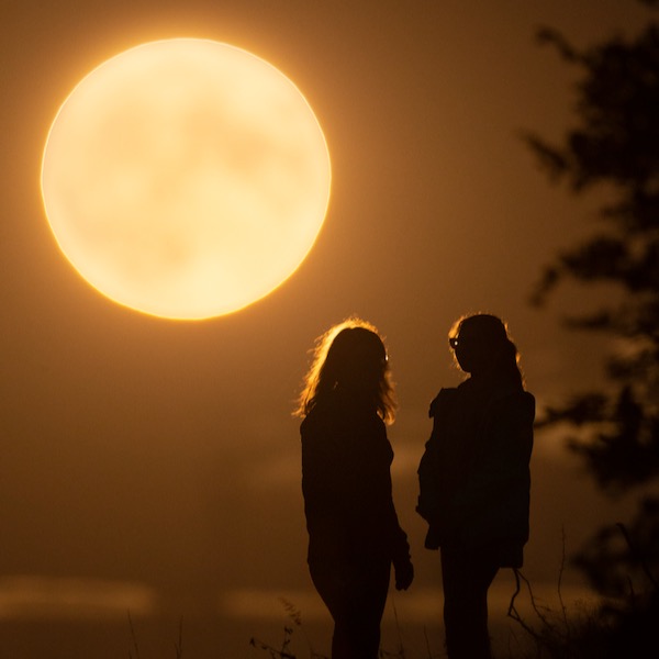 Enormous, bright full moon near horizon with a woman and a girl watching it.