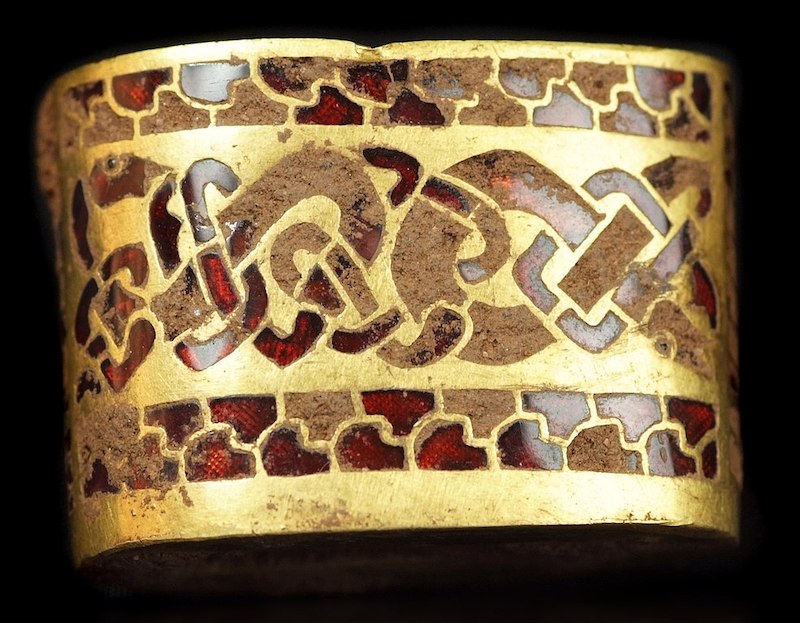 A cuff-like gold object with band of Celtic knots done in inlaid red - the garnets - and brown stone.