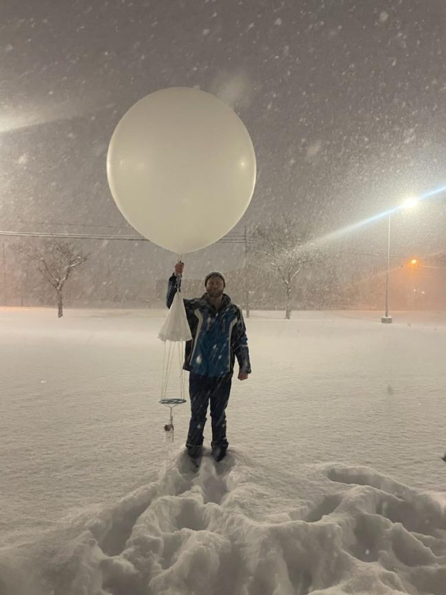 Snowstorms: Man holds large white balloon in falling snow while standing in deep snow.