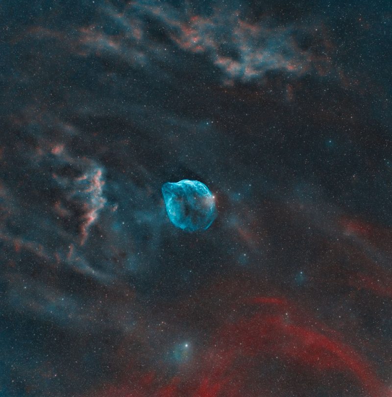 Blue-tinged bubble floating in deep sky blackness with dark cloudy features.